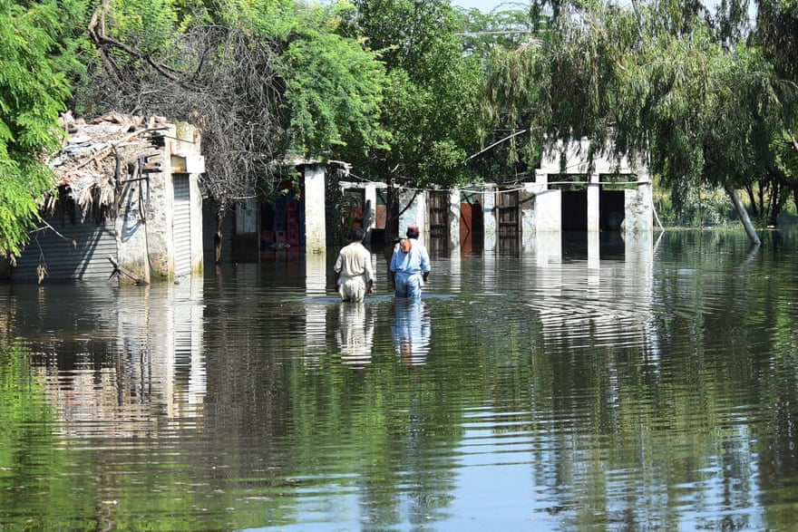 モンスーンによる大雨の後、住民は家の近くで洪水の中を歩いています。