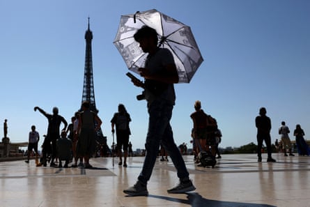 A tourist holding an umbrella to protect himself from the sun walks at Trocadero square next to the Eiffel Tower.