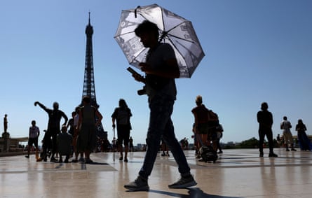 A tourist holds an umbrella to protect himself from the sun at Trocadéro square next to the Eiffel Tower, with other tourists in the background