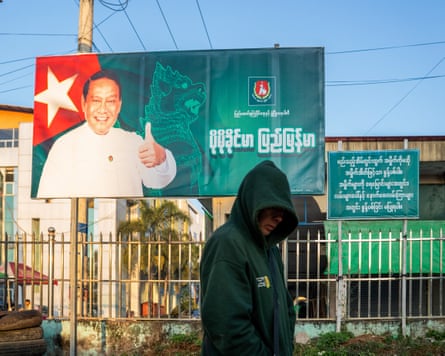 A man in a hoodie walks past an election campaign billboard featuring a smiling man giving a thumbs up