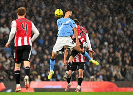 Manchester City's Divine Mukasa and Brentford's Mikkel Damsgaard go up for a high ball in the rain.