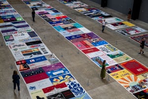 A view from above of people looking at three rows of colourful quilts and panels laid out on a concrete floor