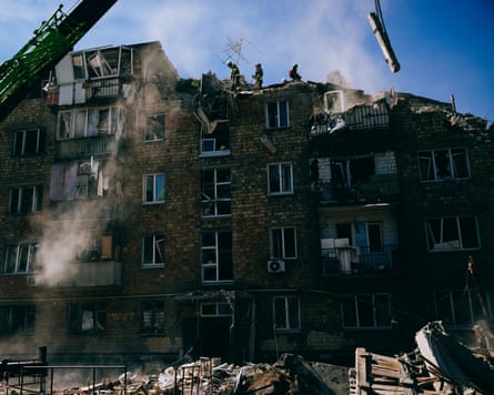 Rescue workers on top of a badly damaged building, crane in view.