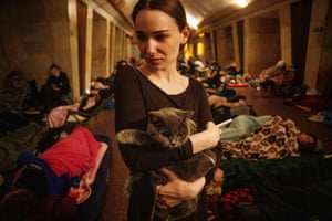 A woman holding a cat with a crowd of people sitting or lying on the ground behind her
