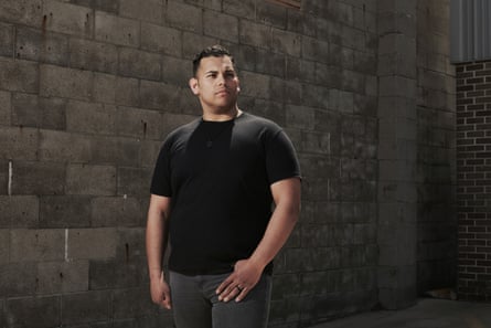 Man in a black shirt stands for a portrait in front of a concrete brick wall