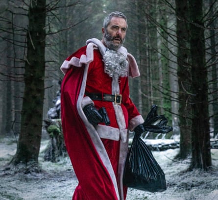 Nesbitt is in the woods, scowling, dressed in a Santa costume, carrying a swag bag and a gun