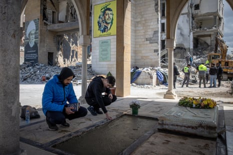 People clear rubble as men pray at the grave of Shiek Sadek al-Nabulsi, who was killed in an Israeli airstrike on the Fatima Al Zahraa complex in Sidon, Lebanon.