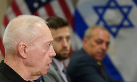 Gallant sits near two men, with US and Israel flags in the background