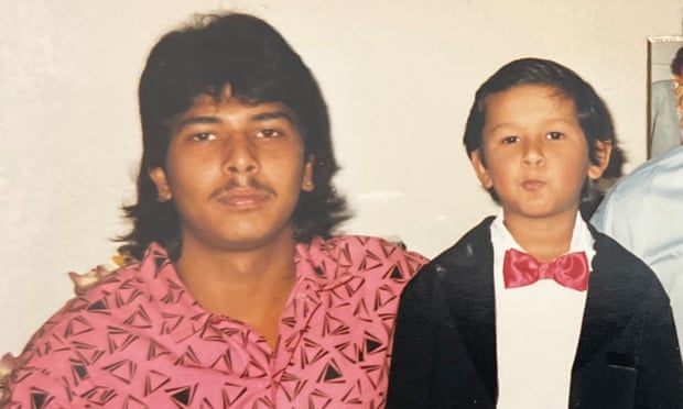 Man wearing a pink shirt, with a mullet next to a child wearing a tuxedo and red bow