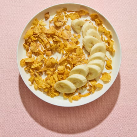 Sliced banana on top of cornflakes in white bowl against pink background