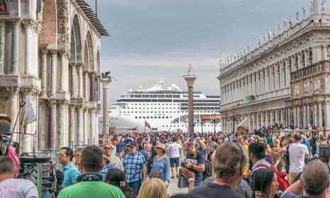A cruise ship at the end of the square at San Marco in Venice which is crowded with tourists between the old buildings