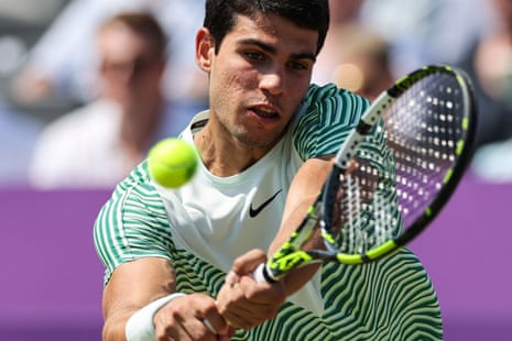 Close-up of Carlos Alcaraz, in the sun, wearing a striped shirt and hitting a tennis ball with his racquet