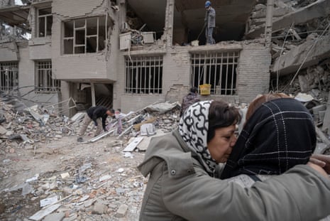 Two Iranian women embrace amid destroyed apartments in Tehran following military strikes.