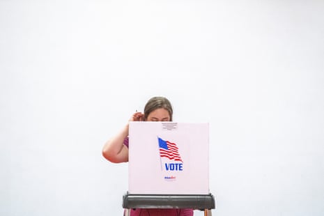 A woman scratches her head while voting behind a cardboard booth reading "VOTE"