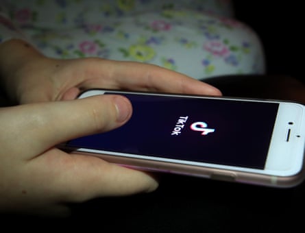 Young person's hands holding a phone displaying the TikTok logo.
