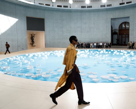 A model in a long bright coat walks down a curved runway