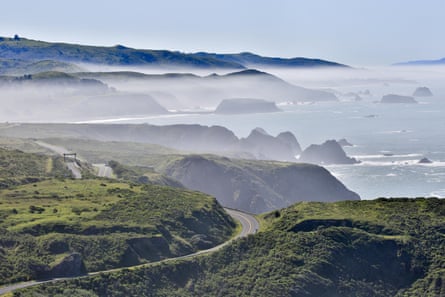 A foggy landscape with green hills dropping into the ocean.