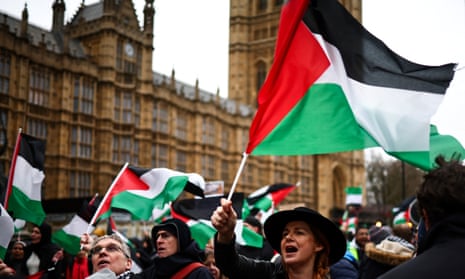 A crowd of people waving Palestinian flags. The Houses of Parliament can be seen in the background.