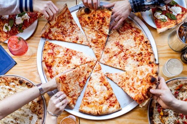 A pizza with hands diving in to share it at Nell’s Kampus, Manchester