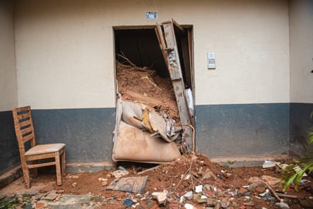 Mud pours through a doorway in an apartment room. The door has broken off its hinges and the dirt reaches almost as high as the door.