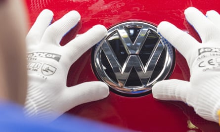 Two white-gloved hands adjust a VW logo on a red car