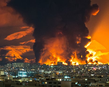 Night time view of flames and smoke rising behind city