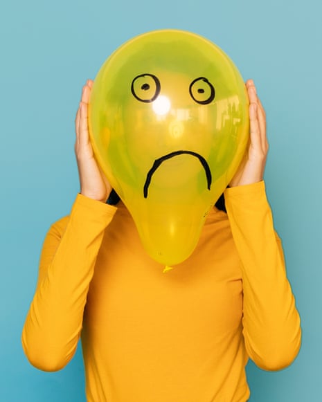 Young woman hidden behind a balloon with a sad face drawn on it