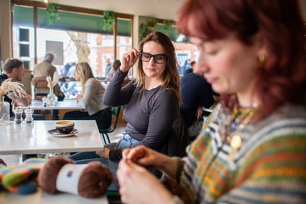 A woman in black-framed glasses looking over at a woman knitting