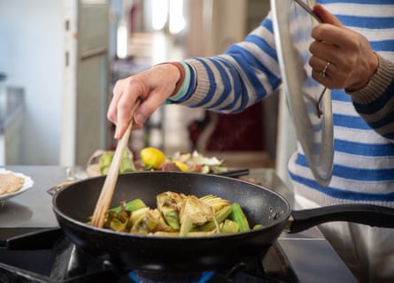 Person cooking artichokes in frying pan