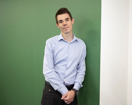 Dan Sexton leaning against a green wall in a pale blue shirt