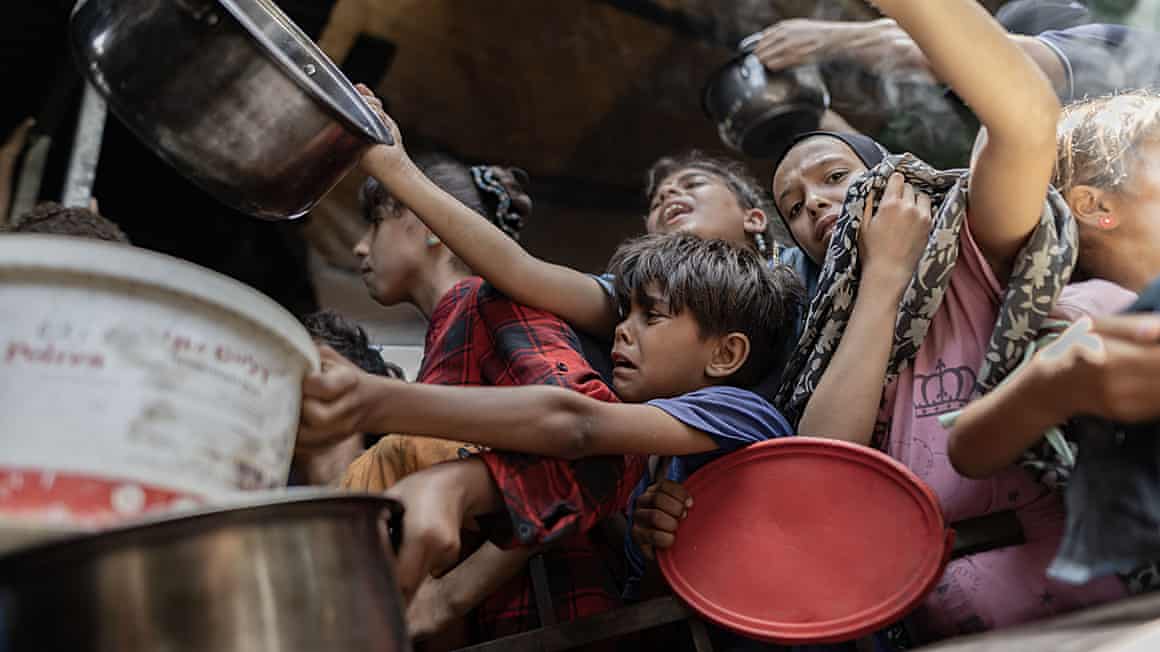 Palestinian children reach out with containers to receive food at Gaza displacement camp