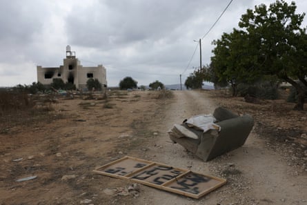 Debris including a sofa lies scattered on a dusty road near a damaged building.