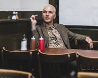 A man with cropped bleached blond hair sits at a table in cafe.