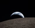 A muted blue Earth with bright white clouds sets behind the cratered lunar surface. (Photo by NASA via Getty Images)