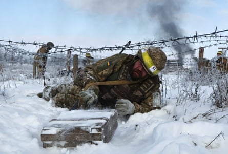 A soldier lies in the snow next to a barbed wire fence