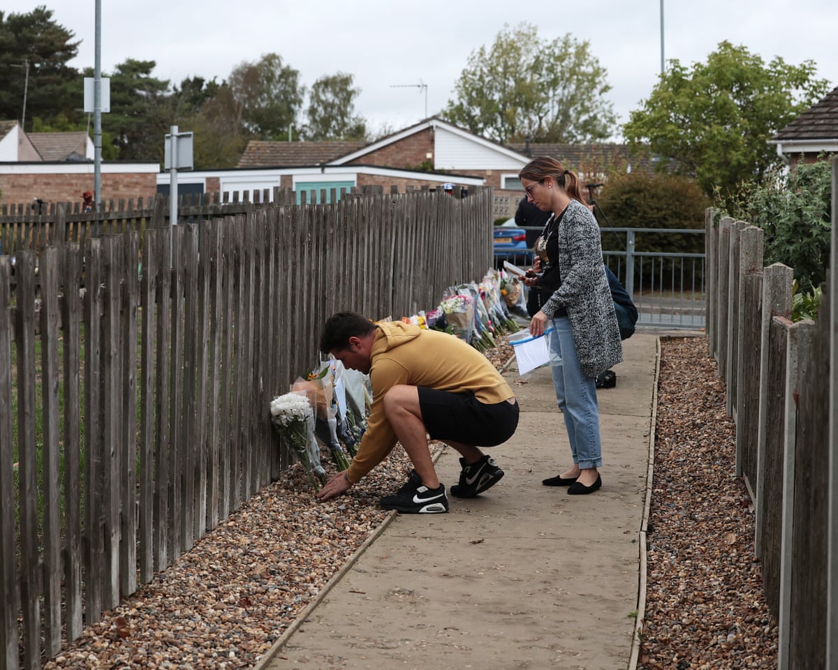 A man crouches down to place a bunch of flowers against the fence as a woman stands beside him