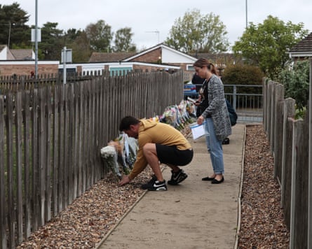 A man crouches down to place a bunch of flowers against the fence as a woman stands beside him