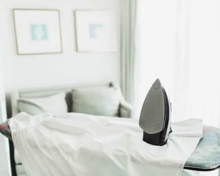 Bright Home Ironing Scene With Steam Iron On Board In Modern Living RoomSteam iron rests on an ironing board in a sunlit living space. The room features a sofa, soft cushions, and framed wall art, suggesting everyday domestic chores and tidy home routines.