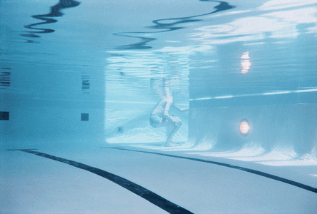 A person crouching at the end of a swimming pool, seen from the other end