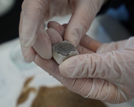 Someone in plastic gloves holds an ancient coin