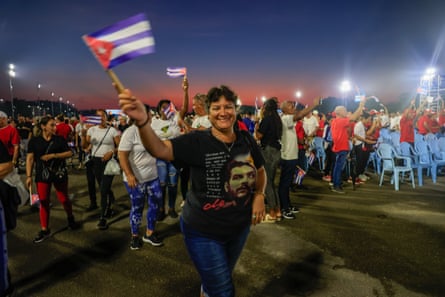 Cubans wave flags attending large outdoor ceremony.
