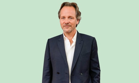 Peter Sarsgaard wearing a navy suit and white shirt, against a mint-green background