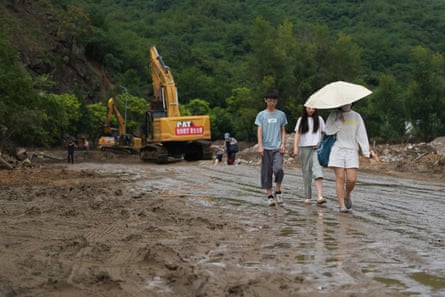 Residents walk across a flood damaged road covered with mud and debris after heavy rains in Miyun district on the outskirts of Beijing.