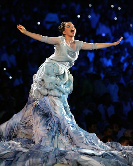 A woman wearing a dress that looks like waves with her arms stretched out and singing