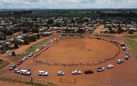 Aerial view of cars and people in a semi-circle on red earth