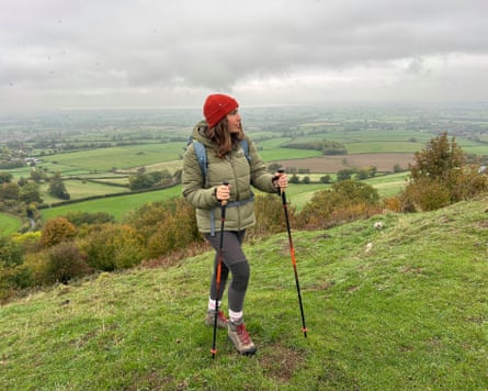 The writer dressed in walking gear with walking poles on a hilltop surrounded by countryside.