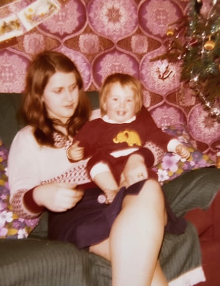 An old picture shows a woman holding a baby in a room with bright pink wallpaper behind them.