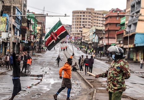 Police officer watches protesters with Kenyan flag during pro-democracy demonstration in Nairobi.