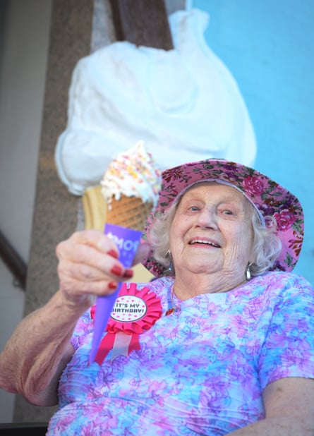 A woman in a hat and a birthday badge, holding an ice-cream cone and smiling
