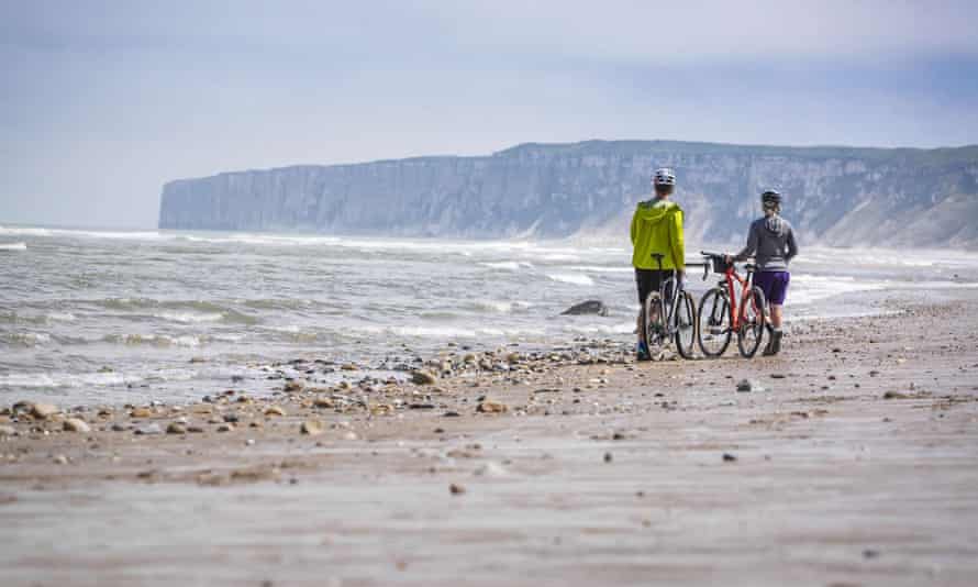 Two figures with bicycles on an empty sandy Yorkshire beach, standing by the sea, a slightly stormy sky